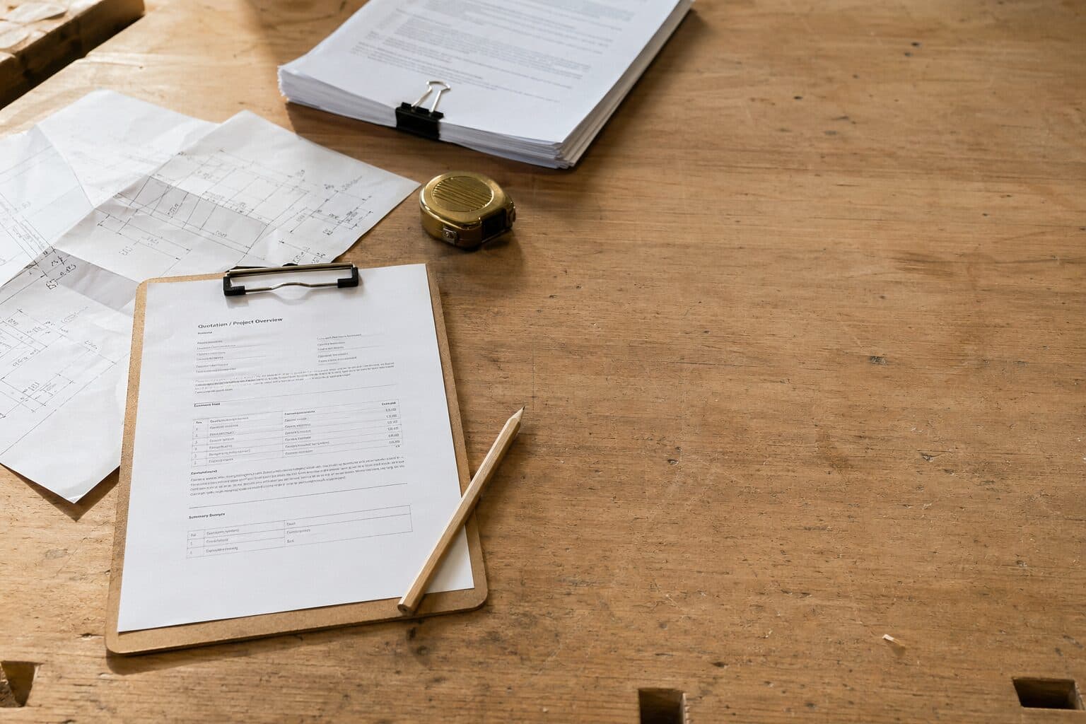 Tømrerværksted med tilbudsdokument på clipboard, målebånd og håndtegnet skitse på robust egetræsbænk